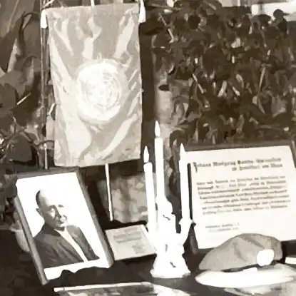 Stilisierter Ausschnitt des Traueraltars: Ein Portrait des Verstorbenen, Kerzen, eine Kappe und eine Flagge.